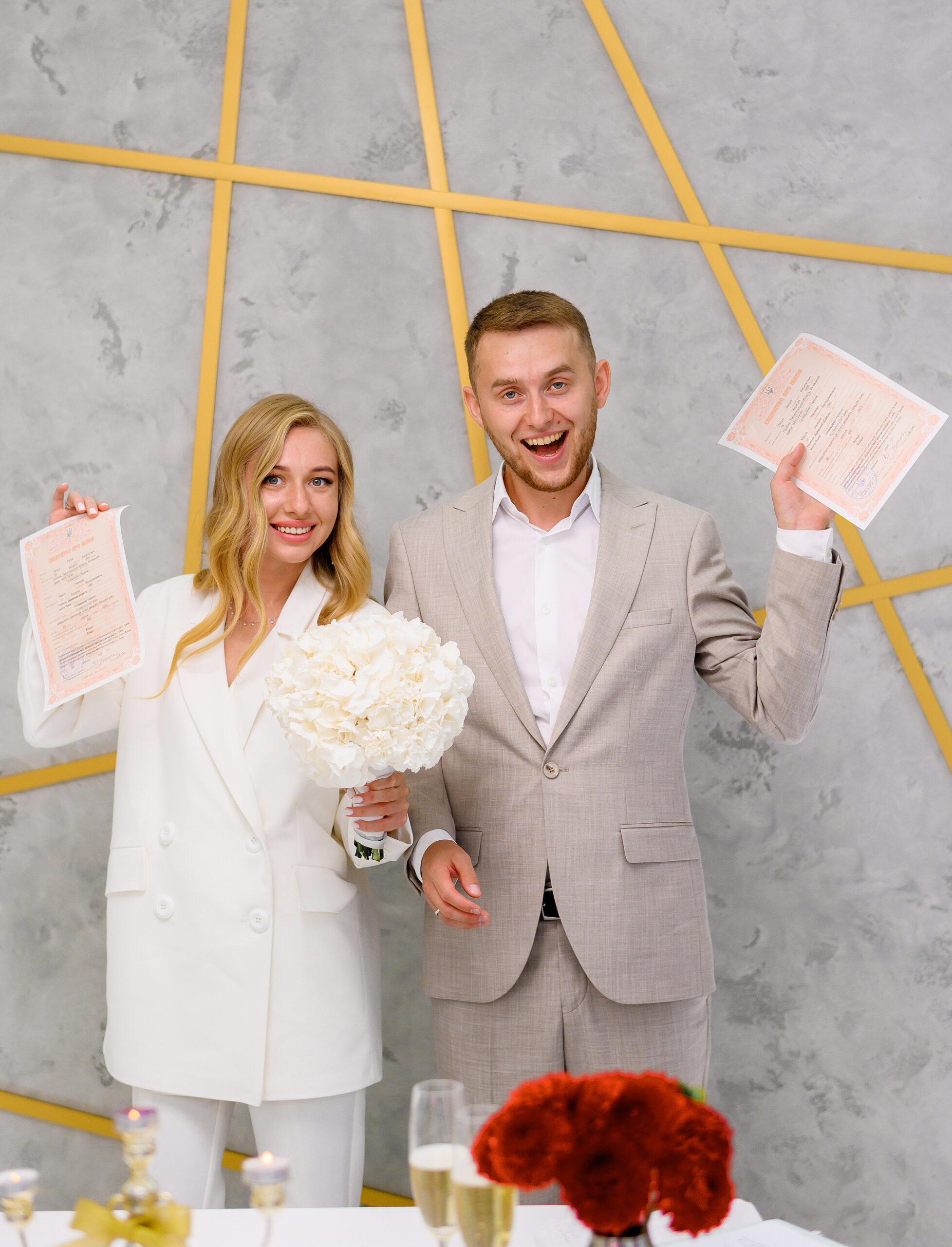 happy attractive married young man woman holding wedding license smiling wedding day ceremony cute blonde bride woman wears stylish white wedding suit family celebration